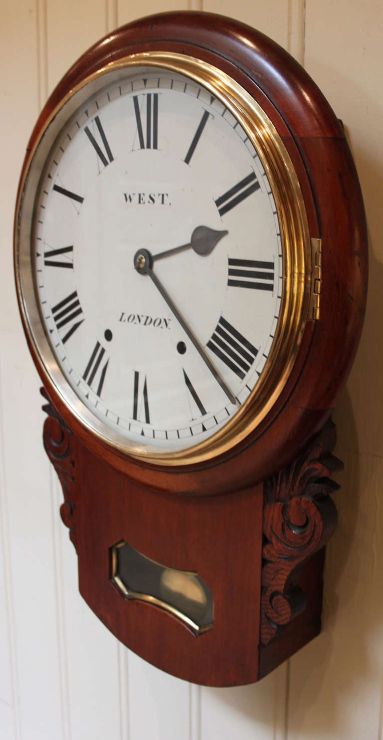 A mahogany cased wall clock, having a drop dial case, with side carvings and a shaped pendulum window. It has a 12