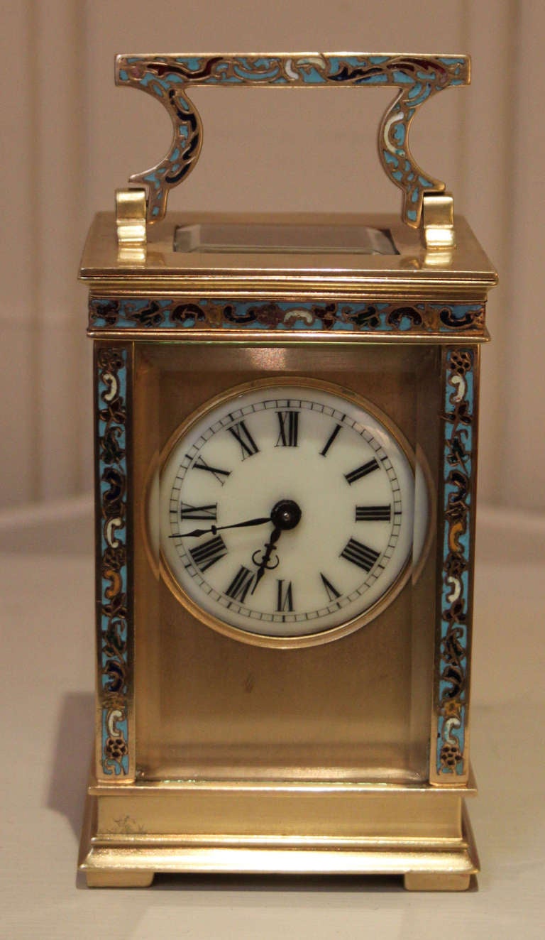 A late 19th Century decorative timepiece carriage clock, contained in a brass case with champleve enamel decoration. It has an oriental style top handle, with enamel bandings and side columns and bevel edge glass. The ivory colour enamel dial has a