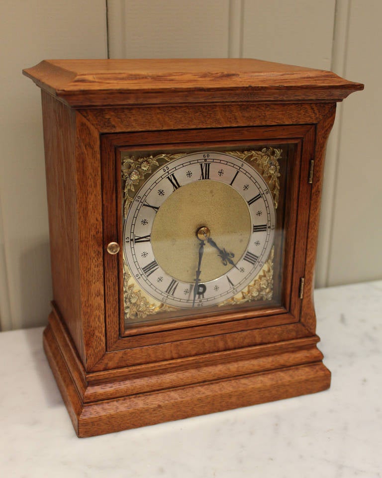 A small solid light oak mantel clock. It has a rectangular case with a flat top with a molded top and base edge. The square brass dial has a silvered chapter ring and brass corner spandrels. It has a good 8 day pendulum movement made by W & H