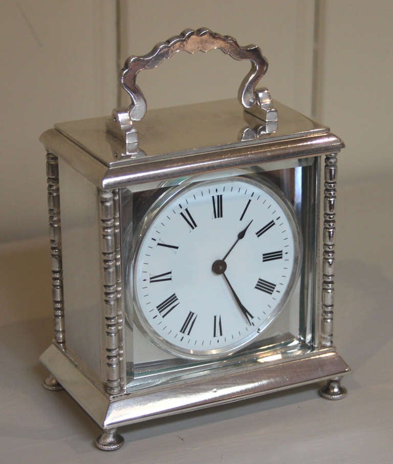 An unusual carriage clock. It has a very heavy silver plated case, with reeded side columns and a wavy top handle. The circular enamel dial is behind a square dial mask and a bevel edge glass. It has an 8 day lever platform movement.