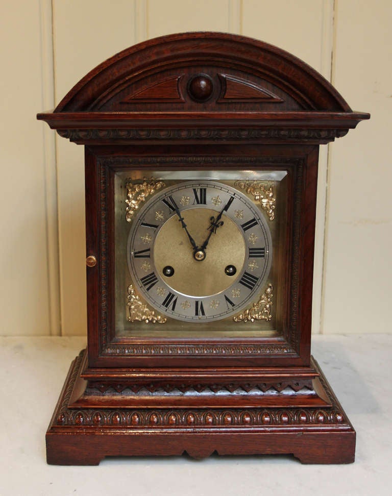 An Oak cased bracket/mantel clock. It has an arch top case with a central turning and an egg and dart moulding to the dial door and base with a shaped plinth. The brass dial has a silvered chapter ring and brass spandrels. The 8 day ting tang