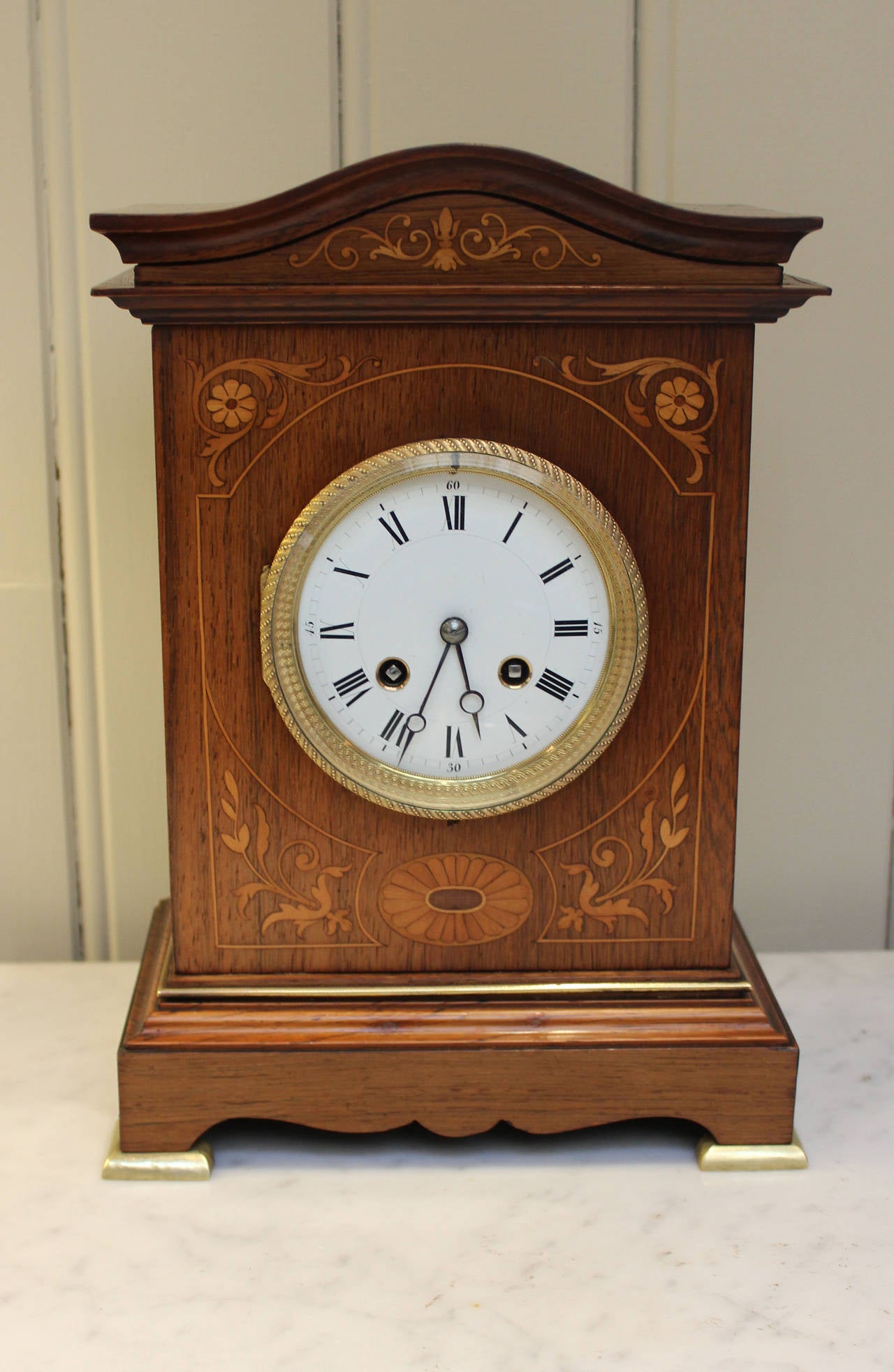 A good quality French mantel clock.The rosewood case has a swept arch top with boxwood and satinwood marquetry inlay. It has a fine cast embossed bezel and inner sight ring with a bevel edge glass and an enamel dial. The 8 day movement strikes the