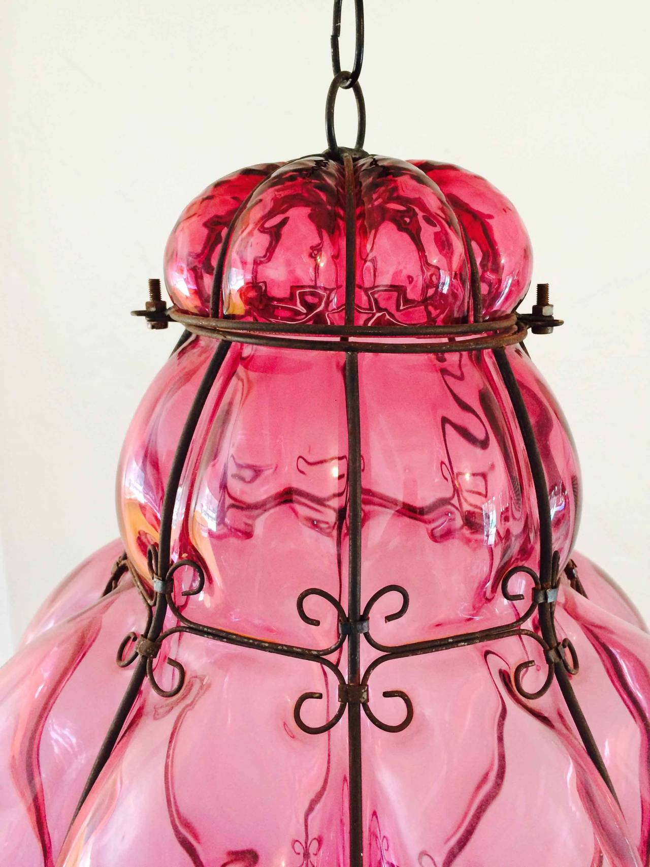 A fine caged Murano glass pendant hanging lantern. Translucent cranberry handblown glass item caged in a black lacquered metal. Top unhinges to place or change candle etc. Item appears previously unused with original Murano foil label intact. Item