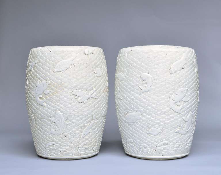 Paire de tabourets en porcelaine blanche finement sculptée, avec des poissons nageant dans des décors de vagues stylisées.