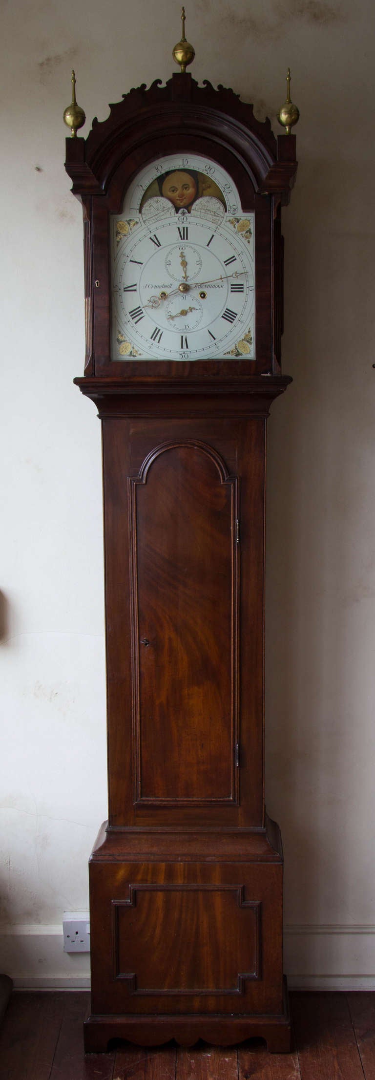 Eight day, weight driven movement with a painted iron dial depicting the phases of the moon in the half-round, break-arch.
Mahogany veneered case with typical Kent clock features; such a the long trunk door with half-round top and delicate cresting