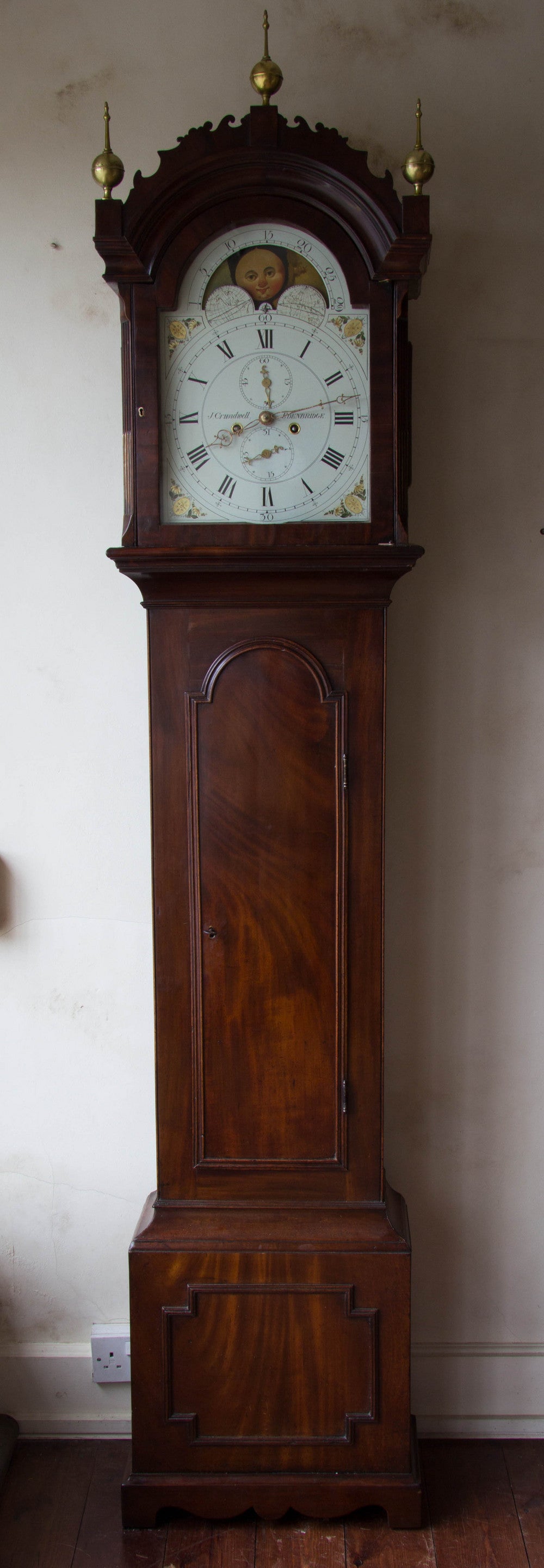 Eight day, weight driven movement with a painted iron dial depicting the phases of the moon in the half-round, break-arch. 
Mahogany veneered case with typical Kent clock features; such a the long trunk door with half-round top and delicate