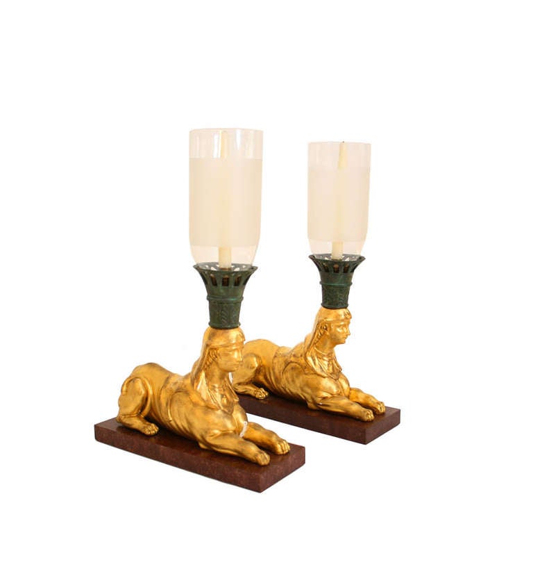 A pair of Regency sphinx-form hurricane lamps, the partially frosted shades set in a verdigris acanthus decorated collar, on gilt sphinx bodies. Porphyry plinth bases replaced.