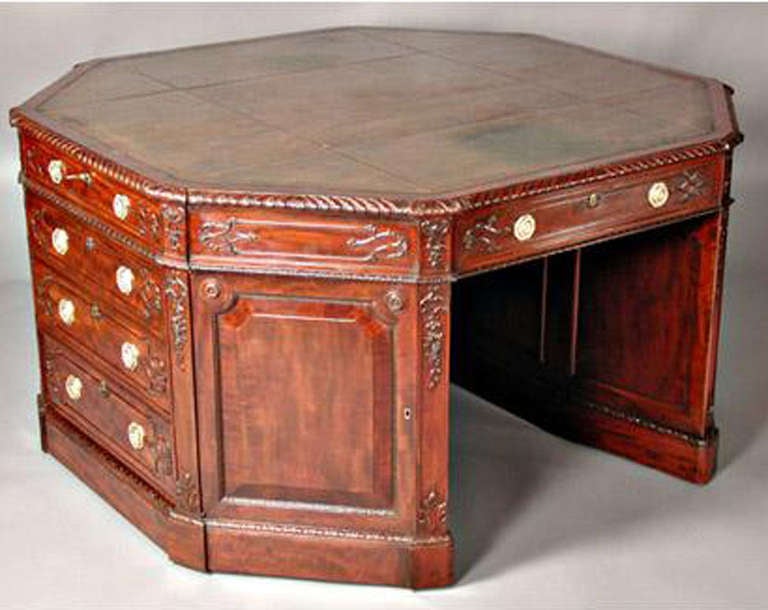 An unusual George III style carved mahogany octagonal partner's pedestal desk, in the manner of Chippendale.  The inset leather top above gadrooned molding above stacks of floral and fret-carved drawers, alternating with paneled doors. Stamped H.