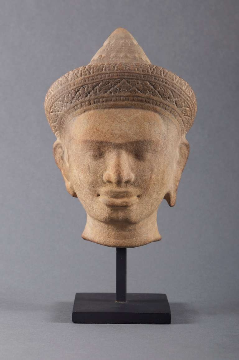 A finely carved sandstone head of a deity, probably Vishnu, with elongated earlobes and an elaborately carved diadem beneath a conical-shaped chignon. The serene countenance with almond-shaped eyes, a broad nose and pouting lips.

The Khmer Empire