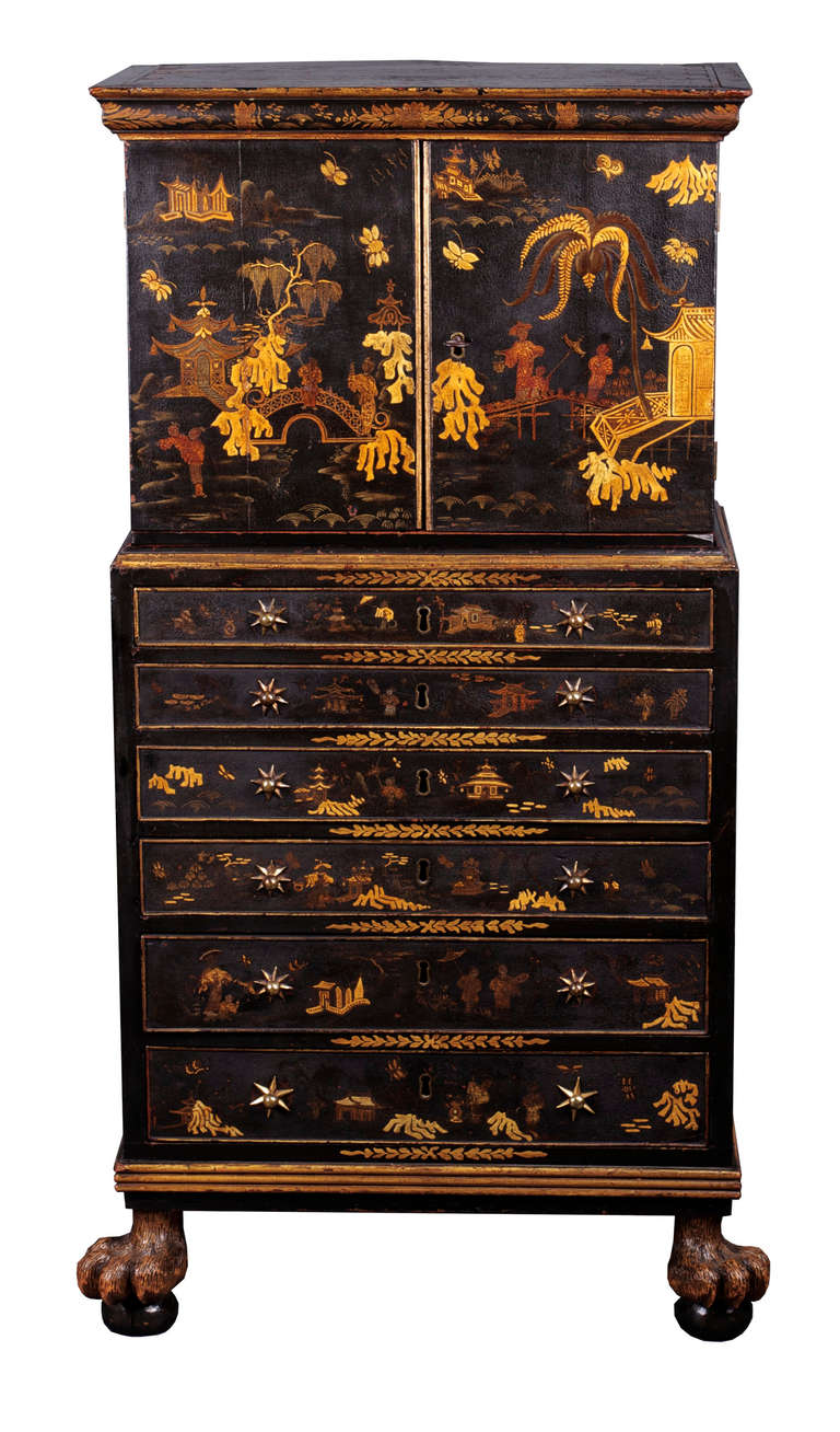 A collector’s cabinet japanned to the exterior with Chinoiserie scenes on a black ground. The upper doors enclosing an earlier Spanish table cabinet interior, comprising nine drawers faced with embossed silver panels decorated with grotesques, the