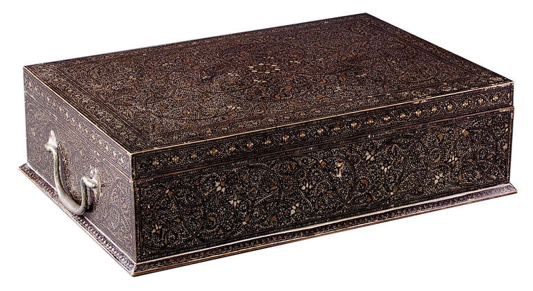 The rectangular steel box profusely inlaid overall with scrolling foliate designs within similarly patterned borders. The hinged lid lifting to reveal a central mirror flanked by reverse-glass flower paintings above an interior with green velvet