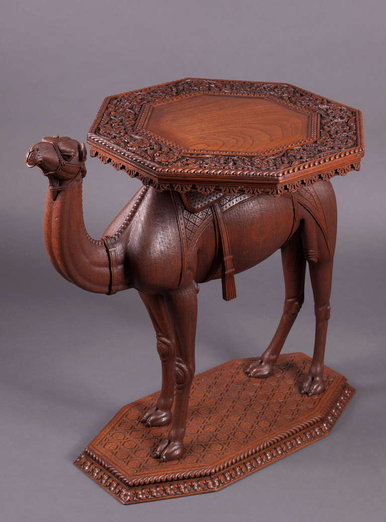 A hardwood side table carved as a camel, the back of the standing camel supporting a table top carved with foliate designs, standing on a carved octagonal base.

Measurements: 28 1/2