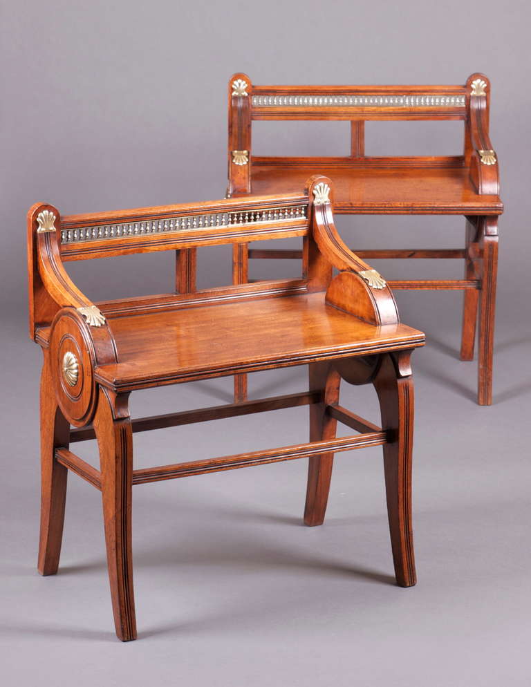A pair of walnut hall benches by James Shoolbred & Co., each with brass mounts, an ivorine label to the underside and bearing two impressed Kite Mark to the reverse. Each comprising a top rail with pierced brass balustrades above a rectangular seat,