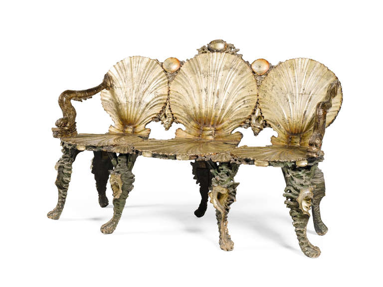 A carved, silvered and gilt-varnished green-painted grotto settee. Comprising a settee with three seats in the form of open scallop shells interspersed with conch and clam shells, arm rests in the form of dolphins and supported on conch shell