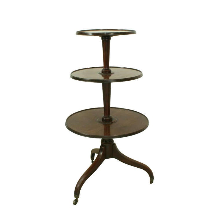 Georgian three-tier mahogany dumb waiter. The round revolving graduating shelves are supported on a turned tapering central column that unites on a tripod base with down-swept curved square tapering legs finishing on brass castors. A fine piece of