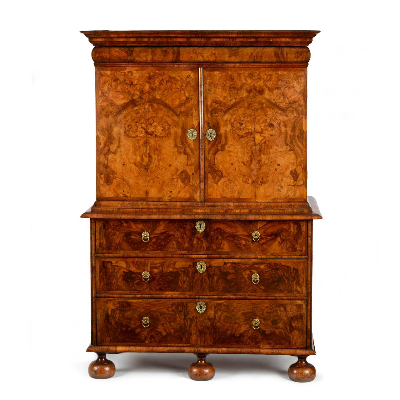 A fine English William & Mary burr and figured walnut cabinet on chest retaining excellent colour and patina throughout. The segmented moulded cornice, over a cushion moulded chart drawer. Below a pair of burr bookmatched veneered doors, with