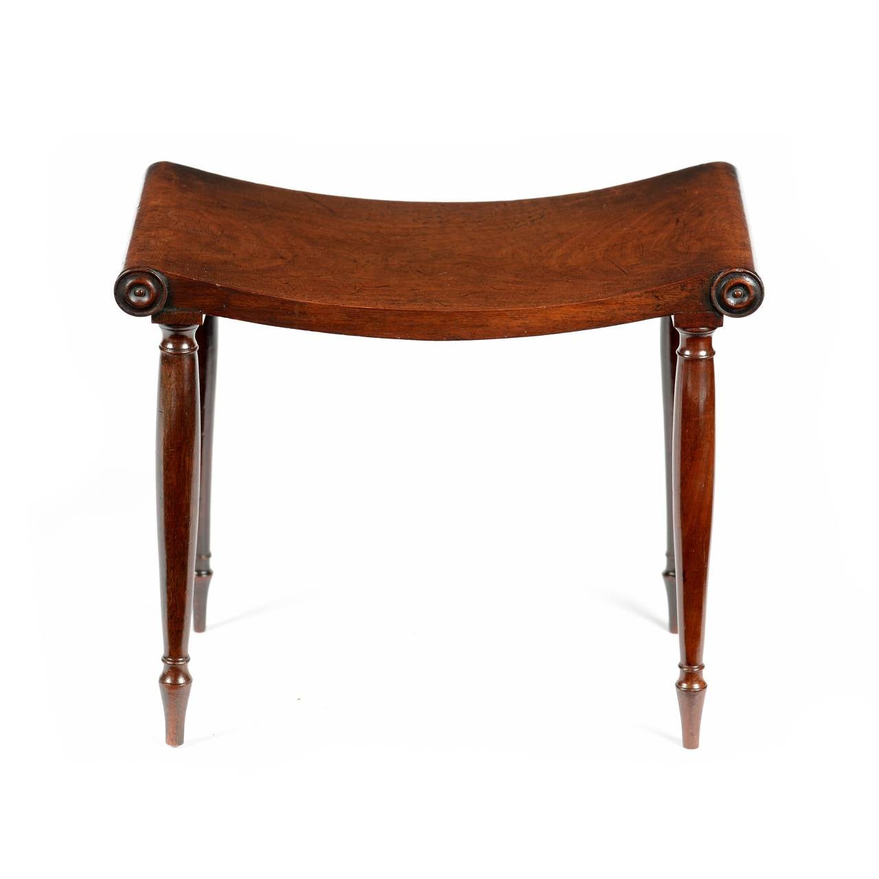 A rare George III mahogany stool in the manner of Marsh and Tatham. The solid mahogany top, shaped in the form of a gentle convex curve, with rounded ends and applied turned roundels. The turned waisted and tapering legs, with a ring turned ankle