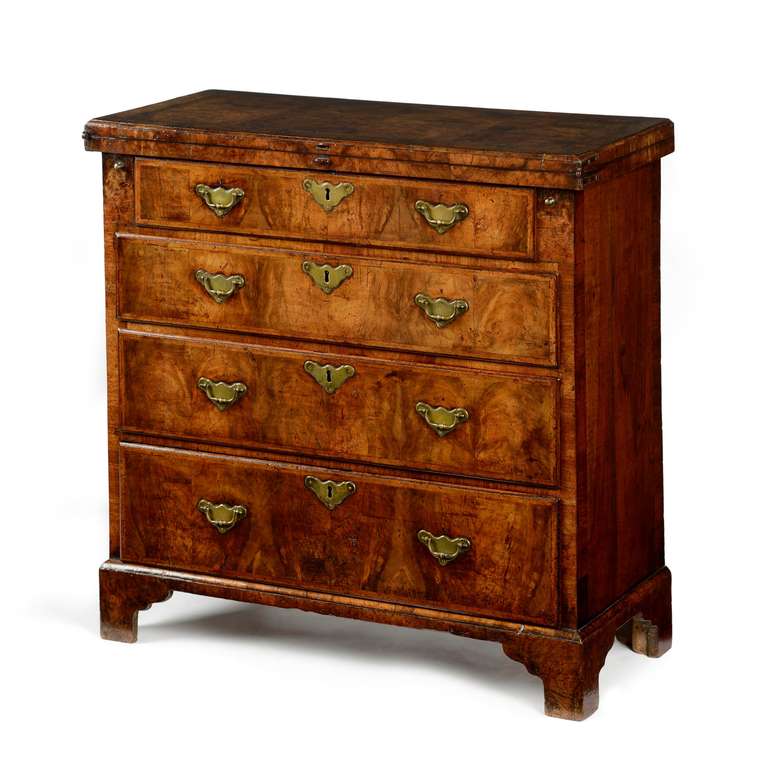 A superb George I figured walnut and feather banded fold over top bachelor chest. The rectangular top with fine figured veneers arranged in a double book match, feather and cross banded, opening to reveal a mirror image arrangement of figured