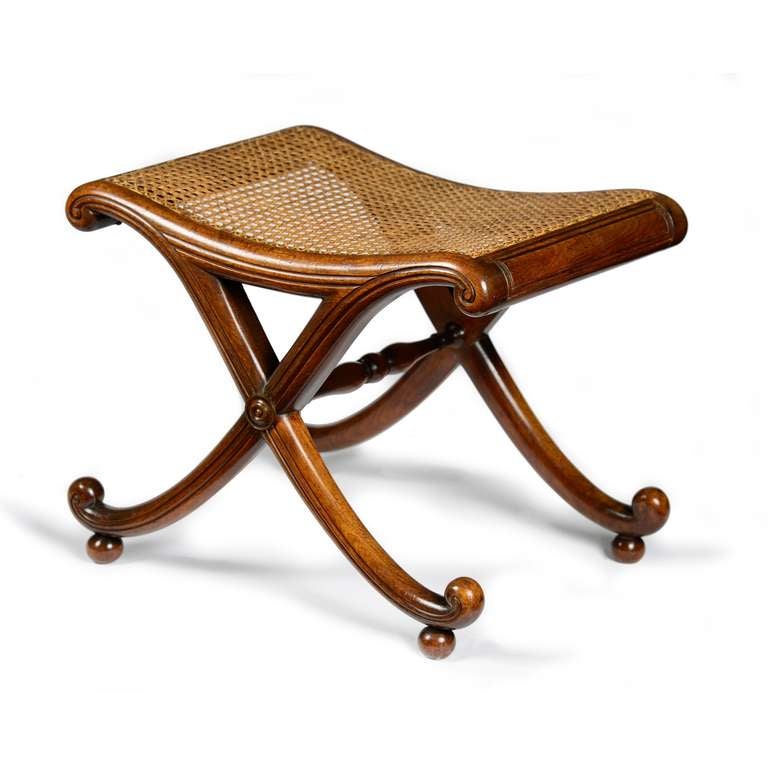A fine Regency mahogany X-frame stool attributed to Gillows of Lancaster. The rectangular caned seat, with serpentine shaped and moulded rails, terminating in a paper scroll to each side, supported by scrolling x-frame legs, united by a turned