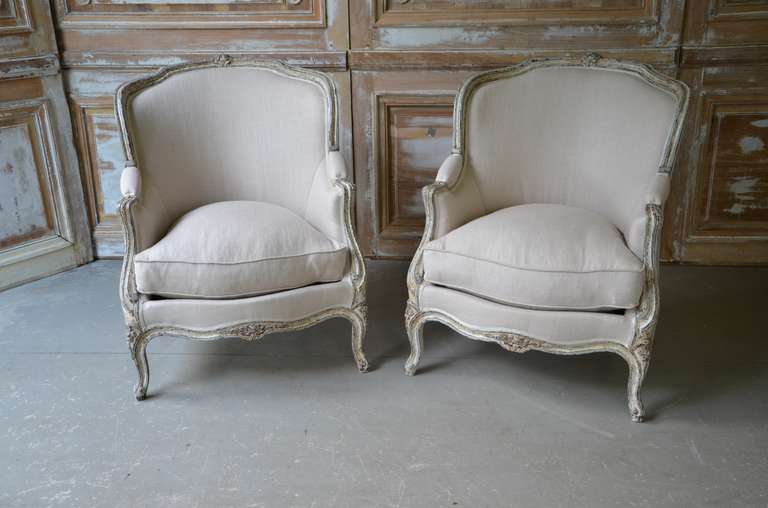 A pair of 19th century French Bergeres in Louis XV style.
The wood frames are in blue-gray painted finish, the top rails decorated with floral crestigs and the seat rails and the cabriole legs with florets. Completely  re-upholstered in linen