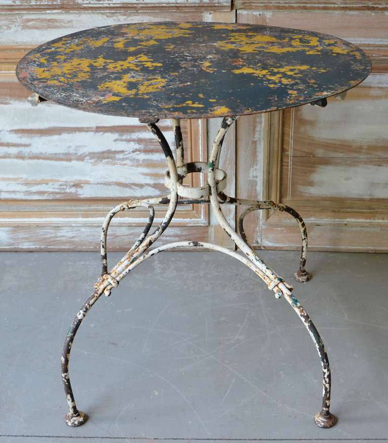 Wrought iron garden table with detailed base and charming patina showing multiple layers of paint.