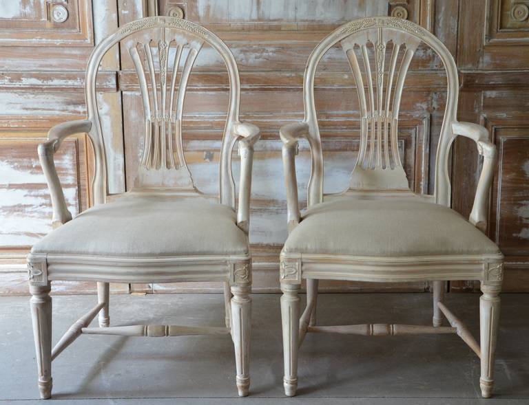 A pair of  Swedish Gustavian style painted arm chairs with pierced slats and carved weatsheaf details, scraped to its ordinal color.

Newly upholstered slip seats covered in linen.

seat hight: 18.50