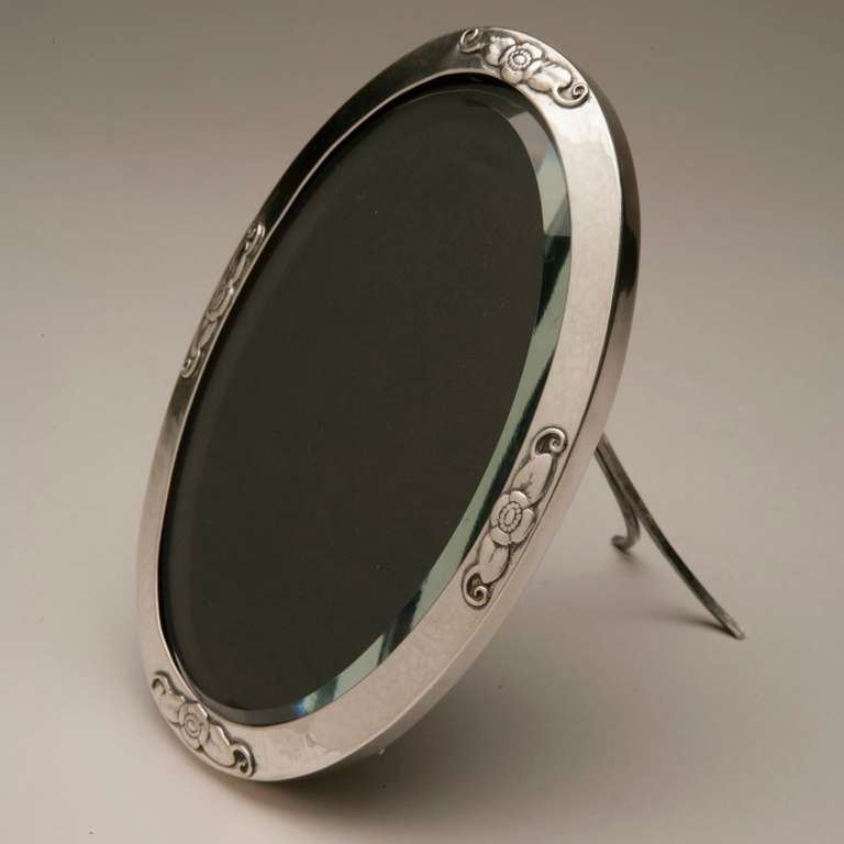 Beautiful sterling silver oval frame with floral motifs. Features a thick, beveled glass piece. and satin backing.
