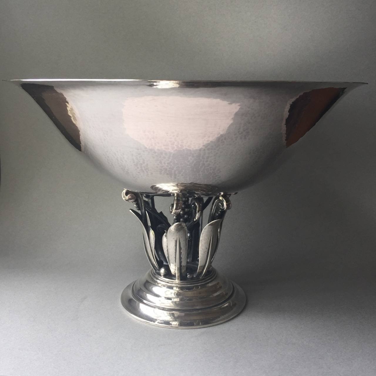 Georg Jensen Sterling Silver Centerpiece Bowl No. 196 by Johan Rohde.

Large silver bowl mounted upon open-worked stem with stylized foliage and clustered cone of berries. Round stepped base. Hand-hammered and chased details.

Early Georg Jensen