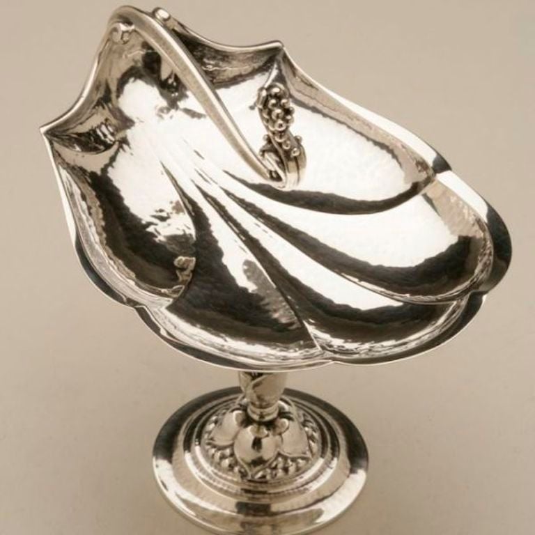 Exceptionally rare Georg Jensen candy dish designed in 1918. On a stepped circular base, rising to a foliate openwork stem, the bowl formed as a stylized hand hammered shell with vine-shaped handle terminating in grape clusters.

Compote dish is