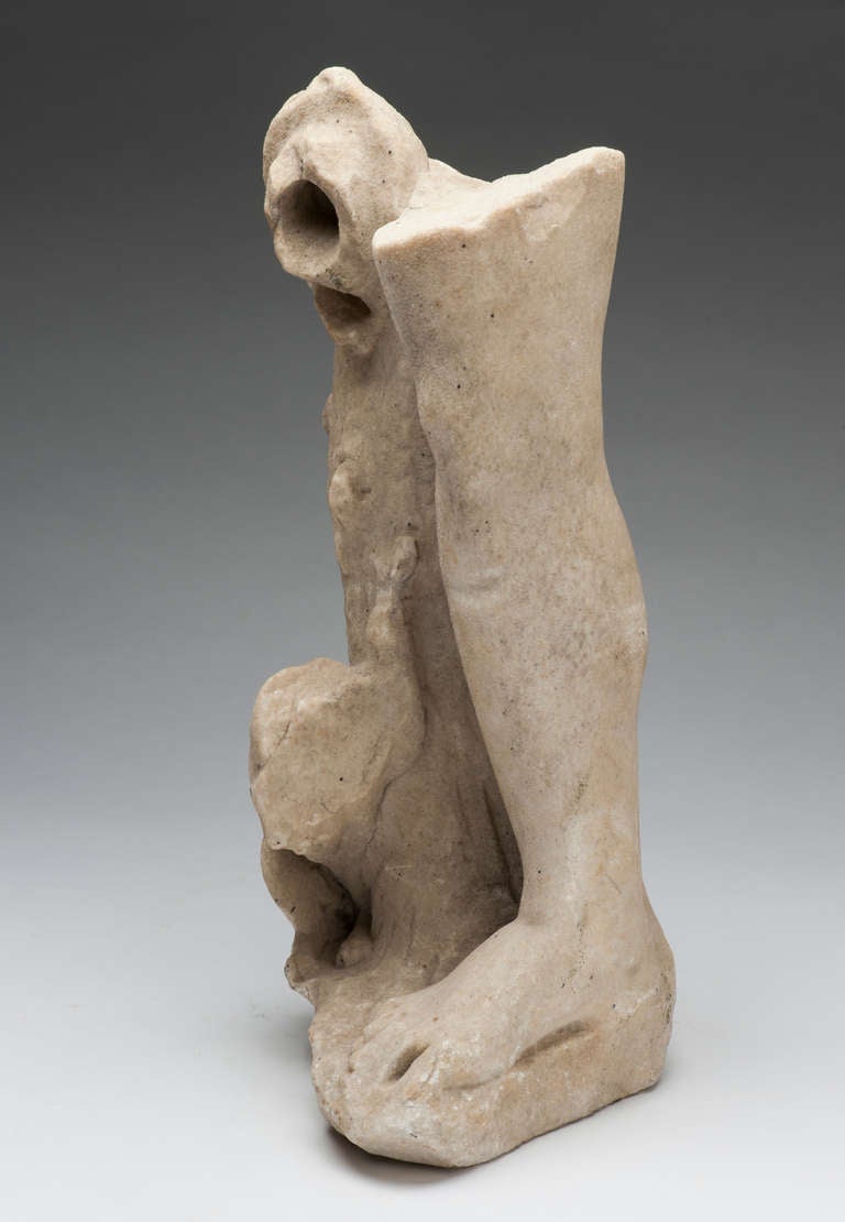 2nd Century A.D. Roman Marble Lower Leg Fragment
14.5 inches tall

The leg and foot are bare.  They stand beside a cut tree trunk topped with a tilted oil lamp and a the lower portion of, possibly, a dog or lion at the base.