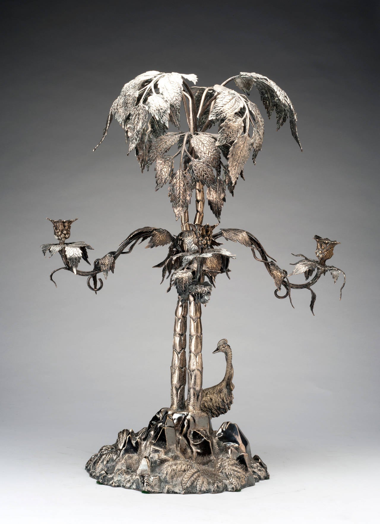 An impressive piece from Elkington Silver, this candlestick accommodates up to four candles on its distinctive arms. The center is crafted in the form of a tree, with a base scene depicting stones, foliage and a flightless bird. The piece measures