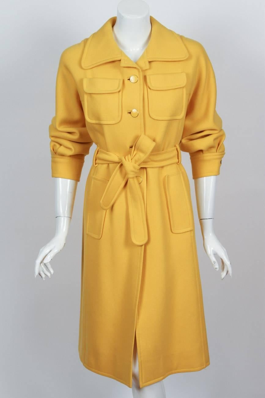 A 1970’s Emanuel Ungaro yellow wool belted coat with yellow ENAMEL buttons and four frontal pockets with a long kick pleat at the back. In excellent condition – missing the yellow enamel disc at the right sleeve button. Size tag 10 but that was