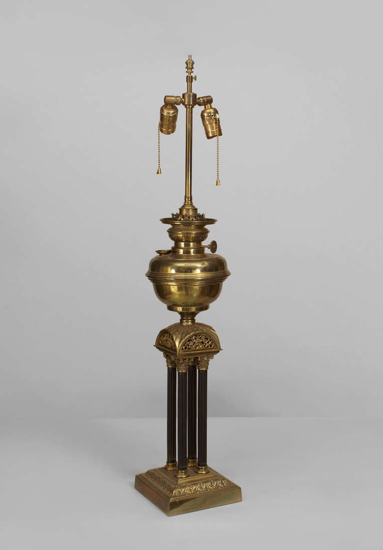 English Victorian brass table lamp with a square base supporting 4 fluted columns under an electrified oil fount.
