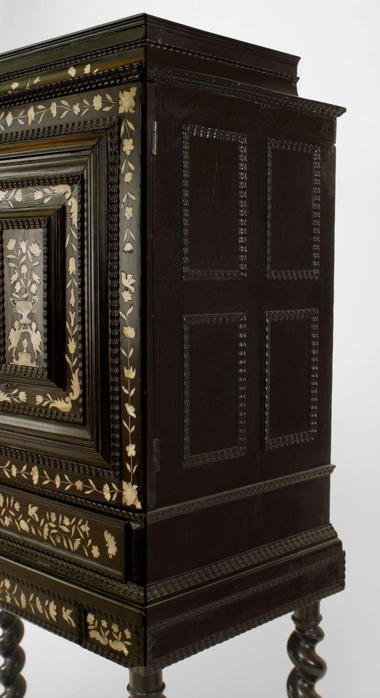 Dating to the turn of the eighteenth century, this Flemish cabinet is composed of ebonized wood inlaid with floral bone trim over four tall swirled legs joined by a forked stretcher. The cabinet's interior features a number of small drawers and