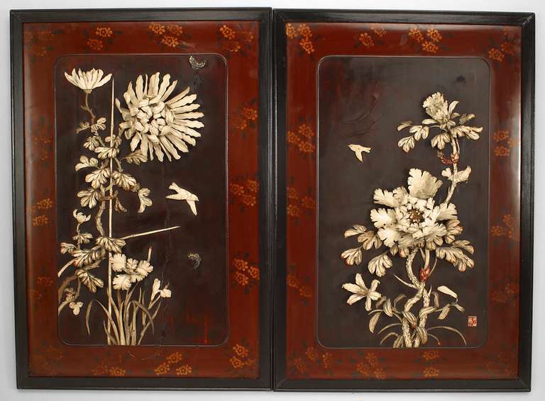 Pair of nineteenth century Japanese ebonized framed wall plaques featuring outcroppings of flowers and bamboo carved in high relief upon a black lacquered palette set within a red lacquered border decorated with painted flowers.