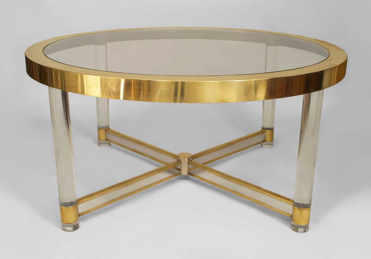French Mid-Century (1950s) dining table having a round glass top inset within a brass rim and supported on 4 round Lucite legs connected by a silver and brass trimmed 