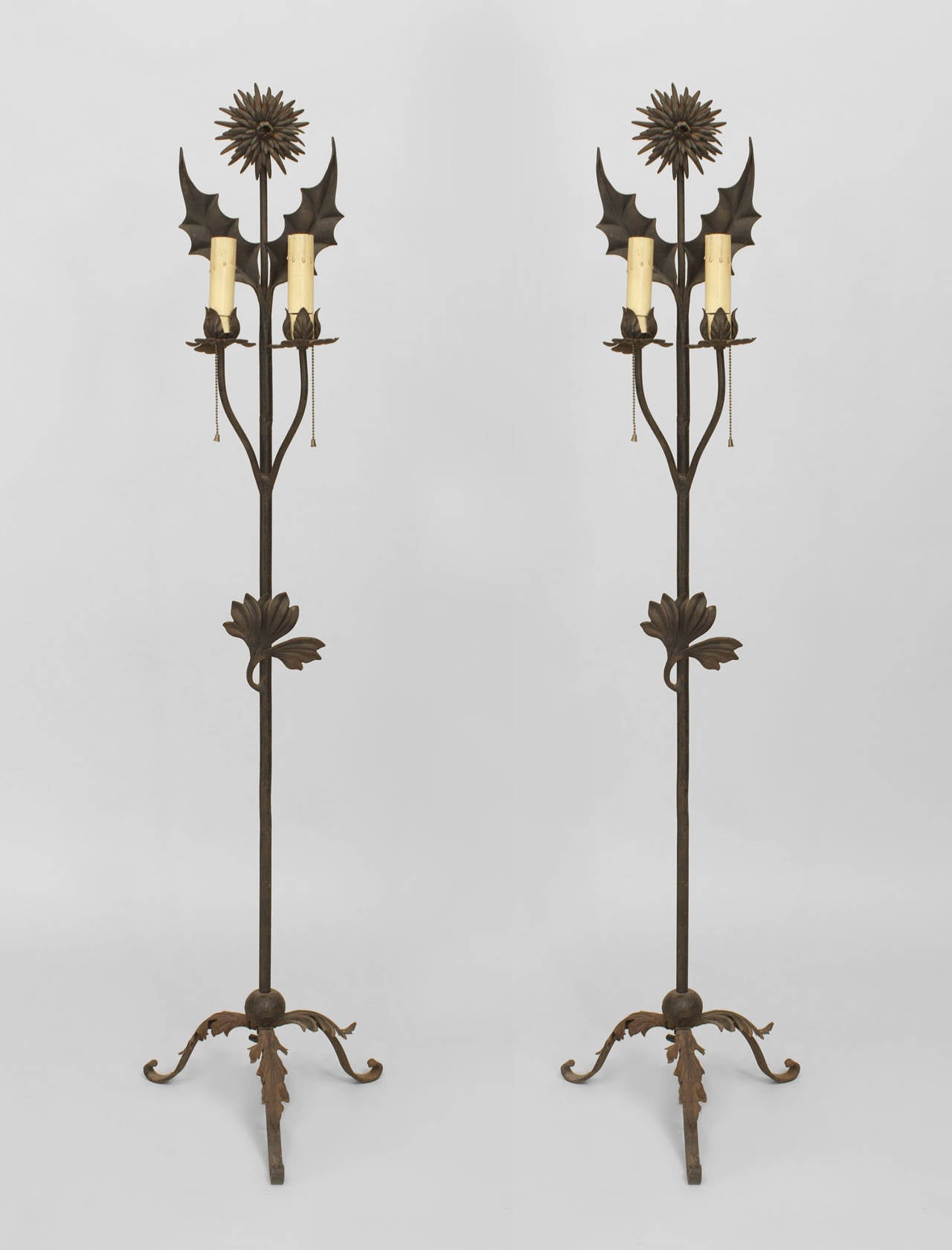Pair of English Aesthetic Movement wrought iron 2 light floor torchieres with a leaf and floral design resting on 3 legs with a sunflower final top (PRICED AS Pair).
