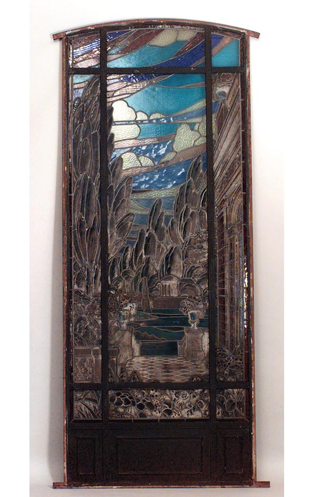 19th century iron framed stained and leaded glass window with an architectural and landscape scene beneath an arch top.