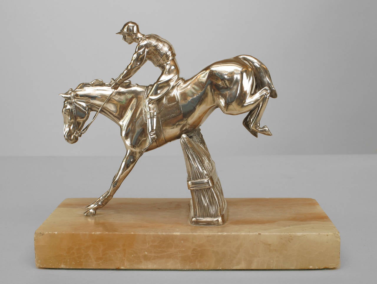 Figurine anglaise victorienne en bronze argenté représentant un cheval et un jockey sautant une barrière en herbe sur une base rectangulaire en onyx blanc.
