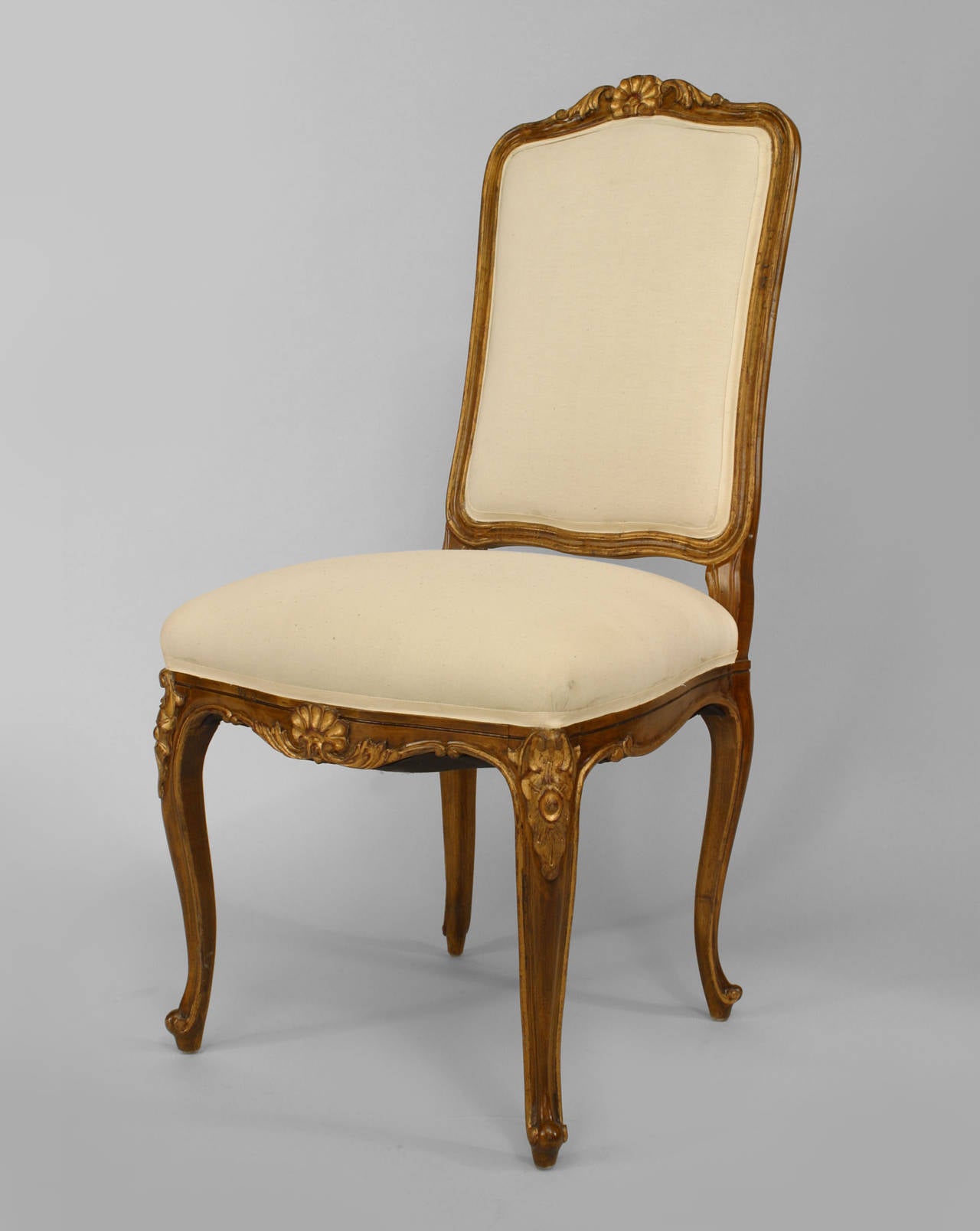 6 Stühle im französischen Louis XV-Stil (19./20. Jh.) aus Nussbaumholz und goldfarben lackiert mit hoher Rückenlehne, muschelgeschnitzter Rückenlehne und weiß gepolstertem Sitz und Rücken.
