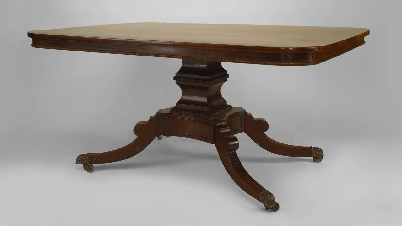 English Sheraton (19th Century) mahogany rectangular dining table with a carved beaded edge apron & supported on a pedestal base with 4 fluted legs ending in brass feet.
