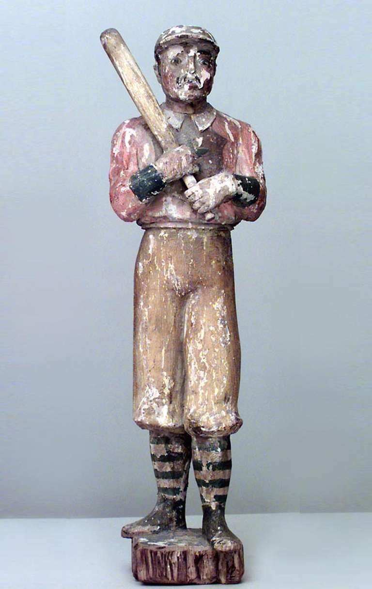 Nineteenth century American Country style carved and painted figure of a uniformed baseball player wielding a bat upon a small round base.
