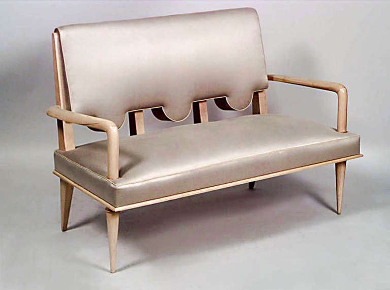 Attributed to noted designer Andre Arbus, this 1940's French sycamore loveseat features a rectangular back carved with three semicircular protrusions at its lower half which are rhythmically divided by four wooden bars where the back and seat meet.