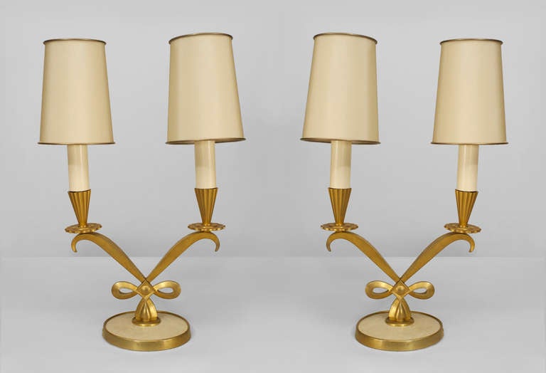 Pair of French Art Deco table lamps each crafted with a pair of curlicued gilt bronze arms supporting two faux candlesticks with round shades, which emanate from a round brass rimmed vellum base.