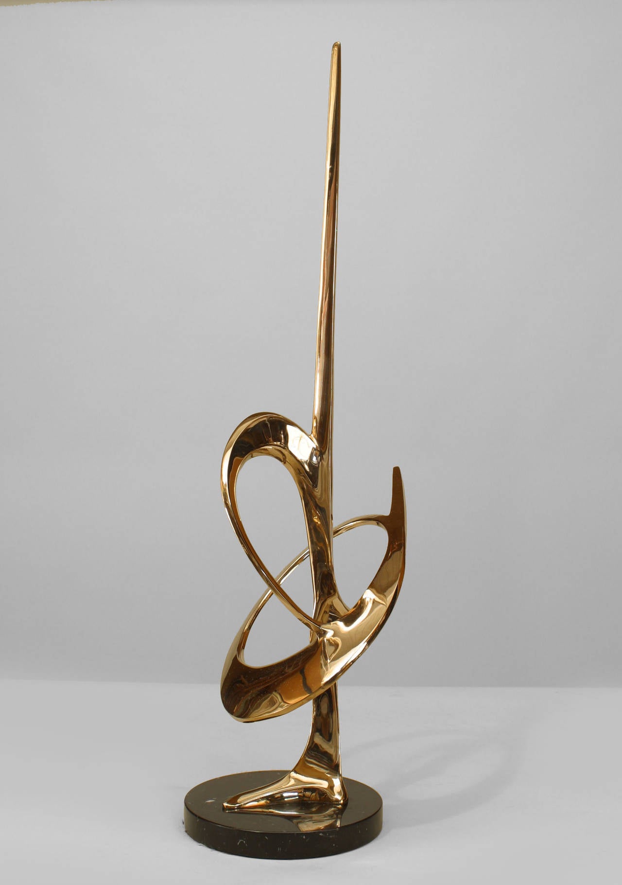 Created by American artist Bob Bennett in 1985, this untitled abstract vertical brass sculpture shows a stylized rod piercing an open oval form on a round black marble base.
