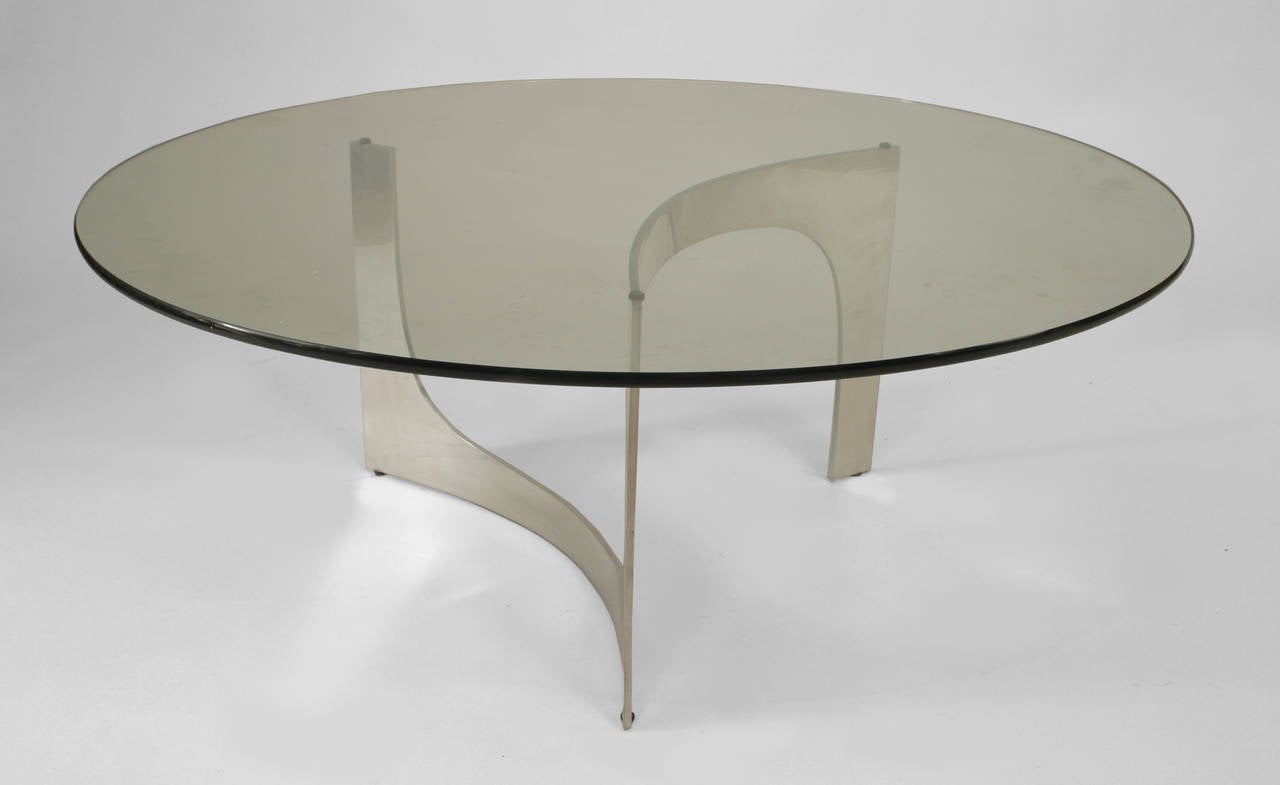 American coffee table with a round glass top resting on an abstract aluminum scroll form base. As is, damage to base.