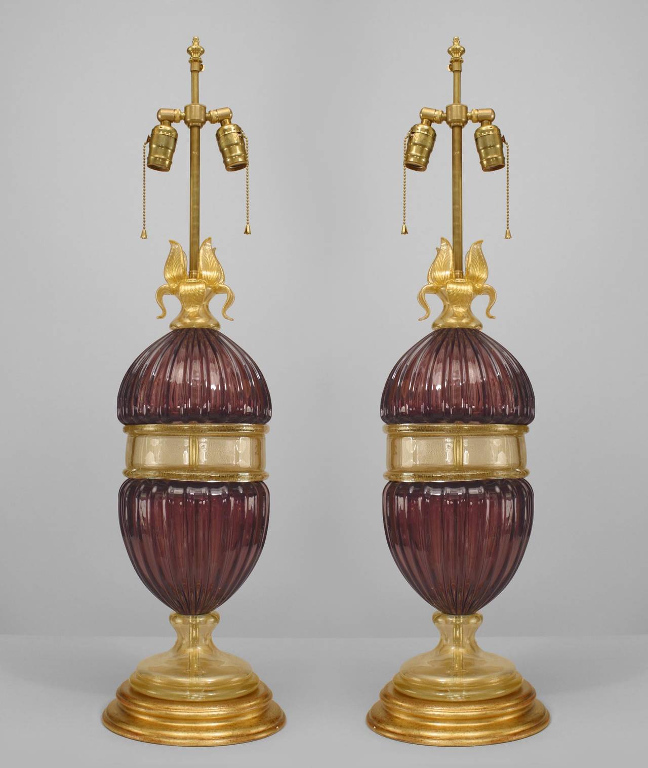 Pair of Italian Murano mid-century style fluted amethyst glass table lamps with a gold dusted glass center section, base and flower top resting on round brass bases (PRICED AS Pair).
  