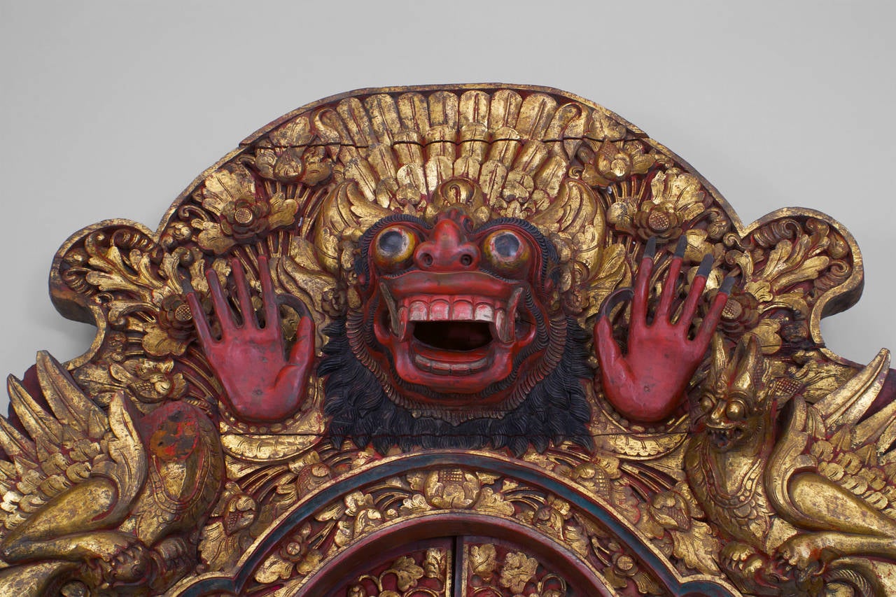 Pair of Asian Javanese (18/19th Century) red and gilt carved temple doors with a large pediment having a head centered by 2 foo dogs with floral carved doors and frame (PRICED AS Pair).
