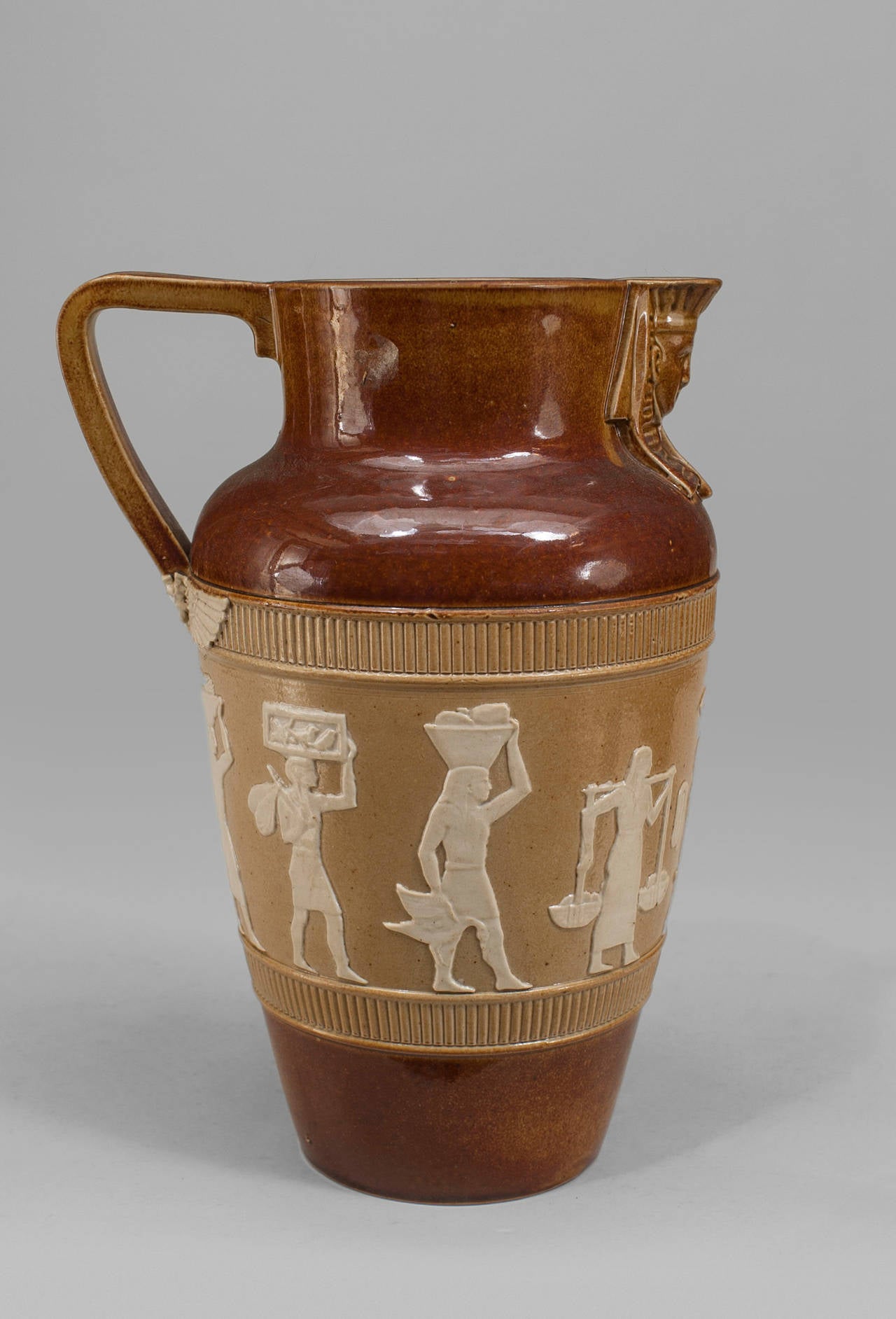 Middle Eastern Egyptian-style (English 1920s) small brown pitcher with sphinx head spout and beige and white classical figures in relief (impressed: DAULTON, LAMBBETH)
