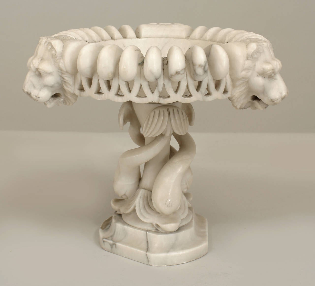 Italian Neo-classic style (19th Cent) white marble tazza form urn with a triangular base of 3 intertwined dolphins supporting a round bowl with 3 lion heads & filigree border.
